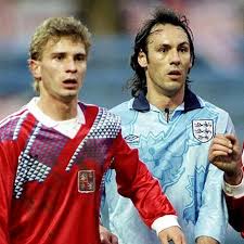 Two football players in action on the field, one wearing a red jersey and the other in a light blue jersey.