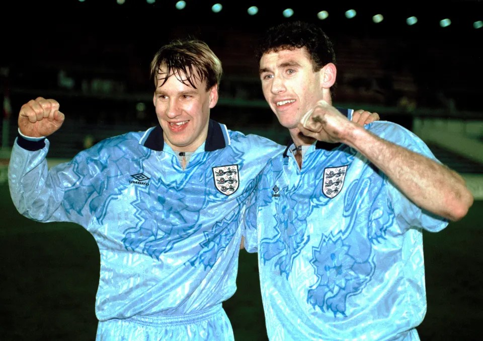 Two football players celebrating together, wearing light blue jerseys with a floral pattern and the England crest.